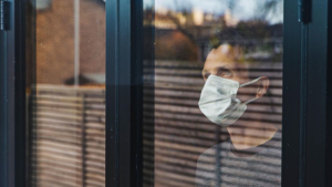 Hombre con mascarilla mirando el exterior a través de una ventana